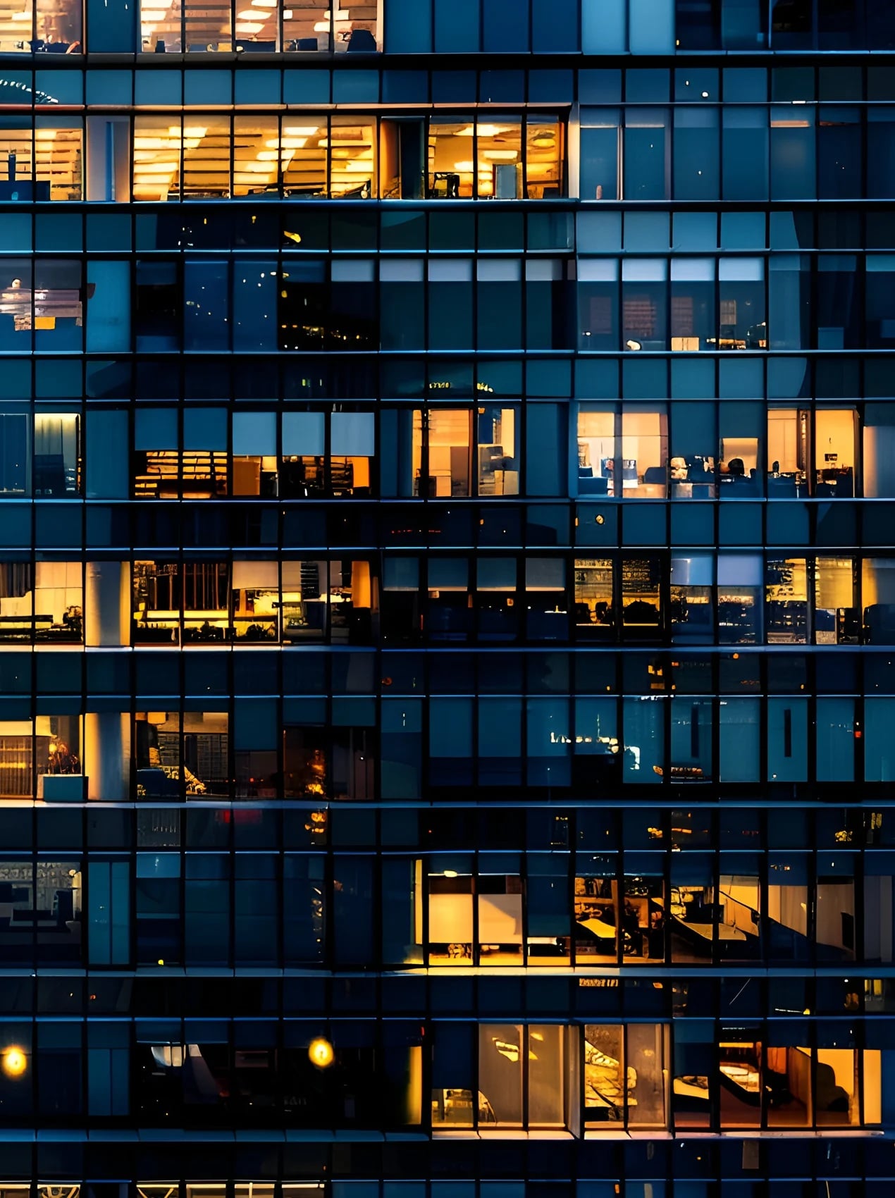 Close-up view of a modern glass office building at night, featuring a grid of blue-tinted windows. 